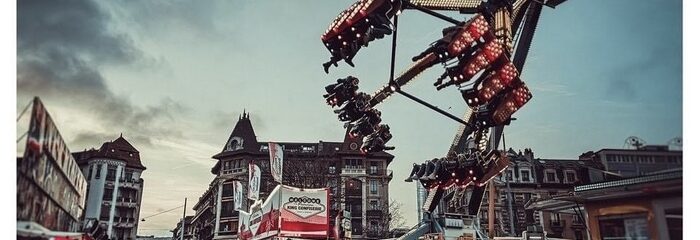 manèges fête foraine avec bâtiments en fond et piétons dessous